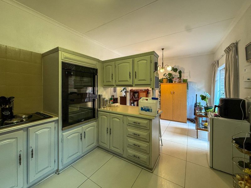A functional kitchen featuring fitted cabinetry, built-in oven, hob, and tiled flooring, offering a dated aesthetic ready for modernization.