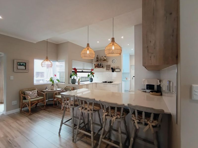 A bright open-plan kitchen and dining area featuring a central island with quartz countertops, modern cabinetry, and warm pendant lighting throughout the space.