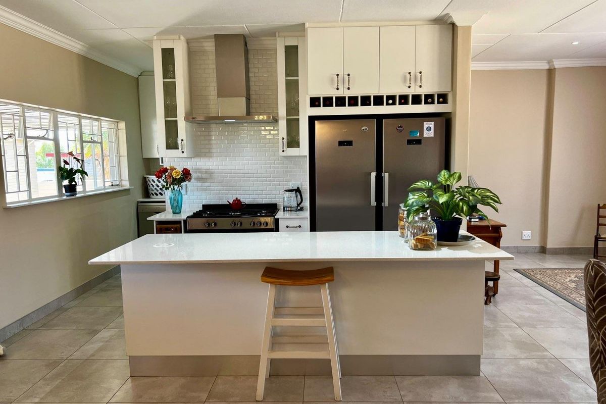 Modern kitchen featuring a central island with stone countertop, white cabinetry, subway tile backsplash, stainless steel extractor fan, and integrated wine storage.