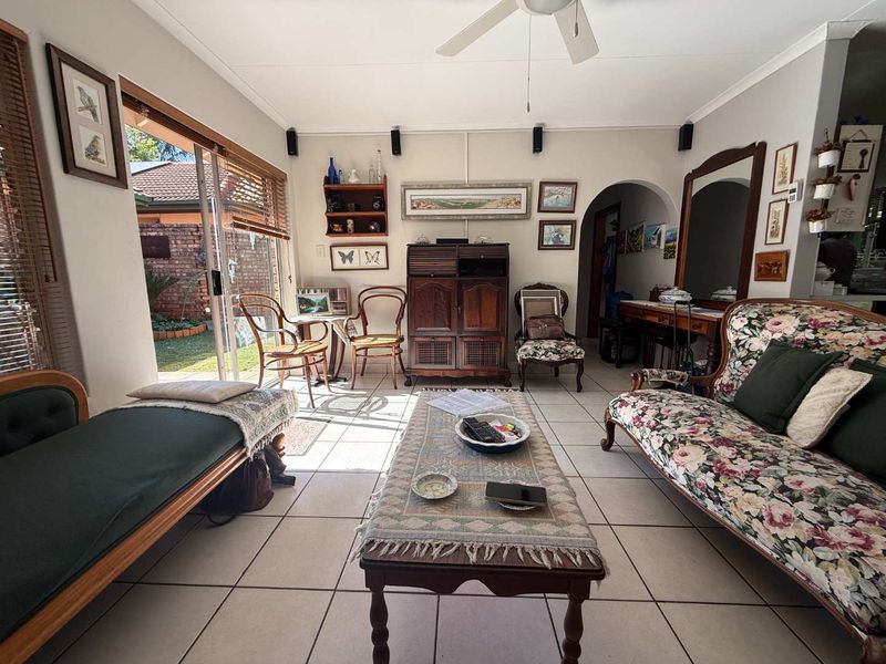 A bright living room featuring ceramic floor tiles, a ceiling fan, and a sliding glass door providing direct access to the rear garden.