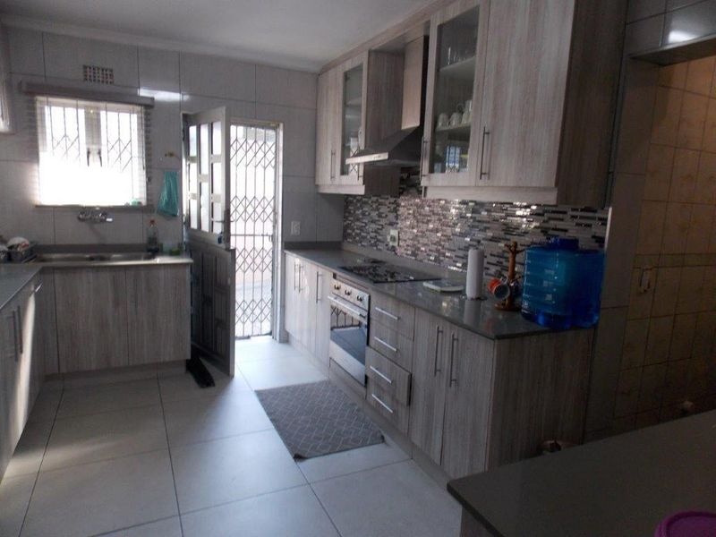 A functional kitchen featuring wood-look cabinetry, stone countertops, a mosaic tile backsplash, and integrated appliances, with direct access to an exterior security gate.