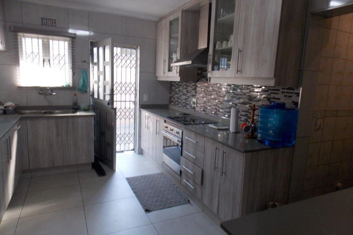 A functional kitchen featuring wood-look cabinetry, stone countertops, a mosaic tile backsplash, and integrated appliances, with direct access to an exterior security gate.