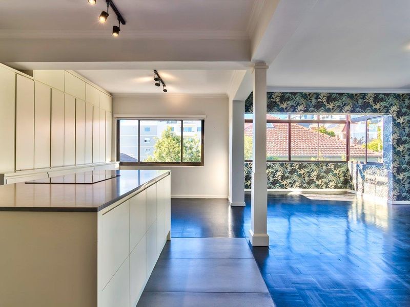 Spacious open-plan living and kitchen area featuring modern cabinetry, a central island, dark timber flooring, and large windows with natural light.