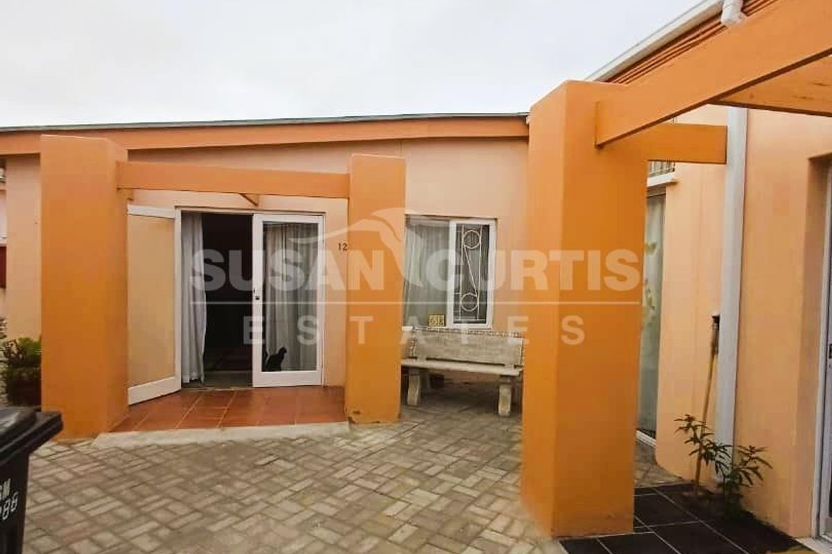 A paved outdoor courtyard area featuring covered patio sections, structural pillars, and direct access to the apartment interior through glass sliding doors.