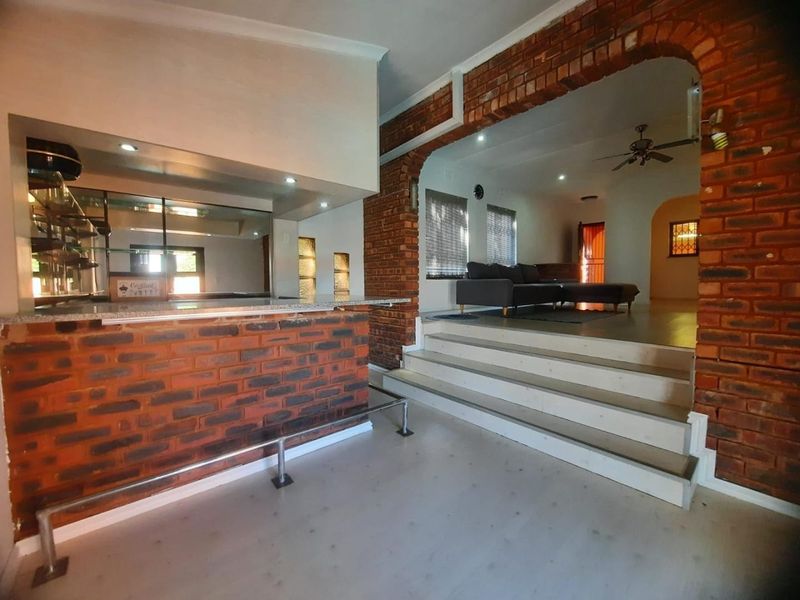 Open plan living area featuring a built-in brick bar, distinctive brick archway, and a raised floor level leading to the lounge space.