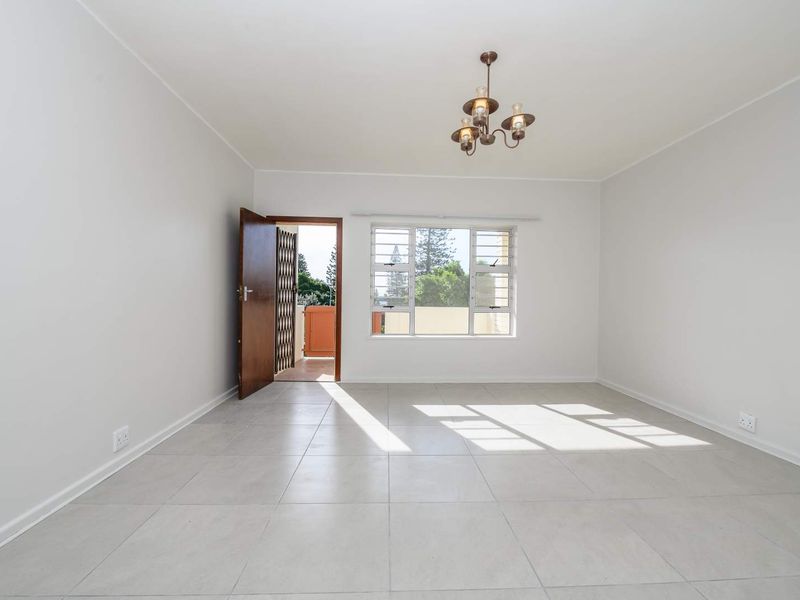 A bright, empty living room featuring neutral tiled flooring, a central light fixture, and access to an outdoor balcony area.