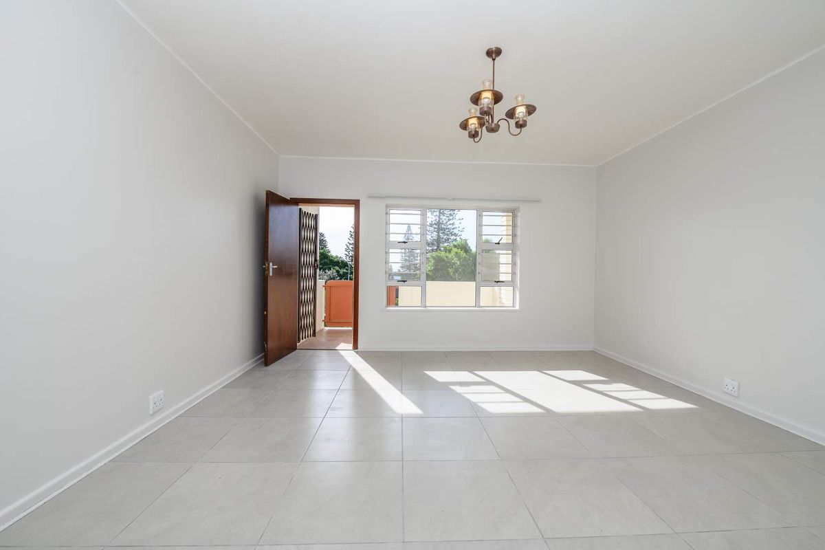 A bright, empty living room featuring neutral tiled flooring, a central light fixture, and access to an outdoor balcony area.