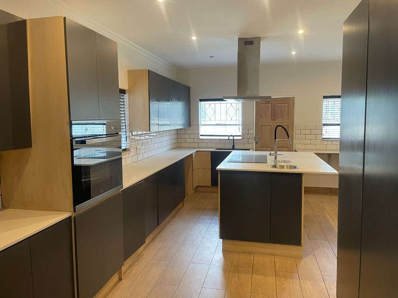 Modern kitchen featuring a central island, built-in oven, extractor fan, quartz countertops, and subway tile backsplash with wood-look tile flooring.