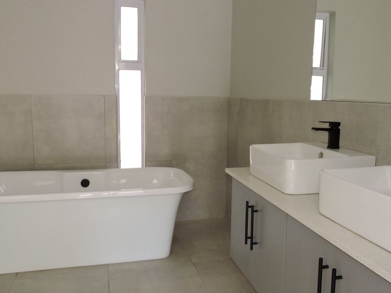 Modern bathroom featuring a freestanding bathtub, double vanity with vessel sinks, matte black fixtures, and neutral large-format wall and floor tiles.