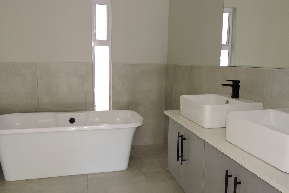 Modern bathroom featuring a freestanding bathtub, double vanity with vessel sinks, matte black fixtures, and neutral large-format wall and floor tiles.