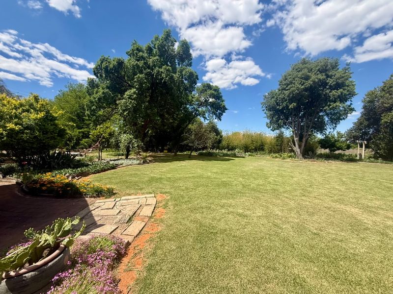 A well-maintained, expansive garden featuring a manicured lawn, mature trees, and a paved stone walkway.