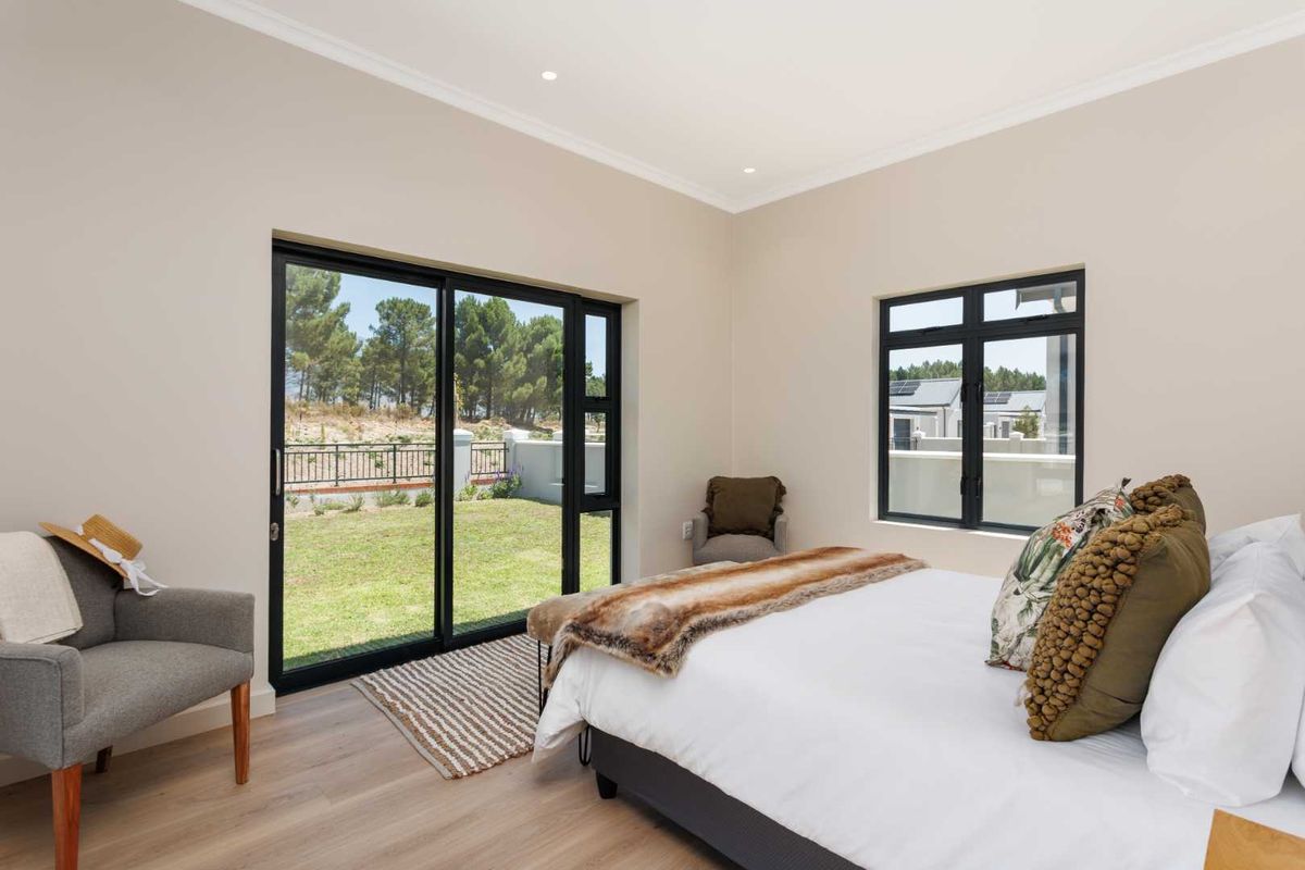 A bright and modern bedroom featuring laminate flooring, recessed lighting, and large black aluminium sliding doors providing direct access to the garden.