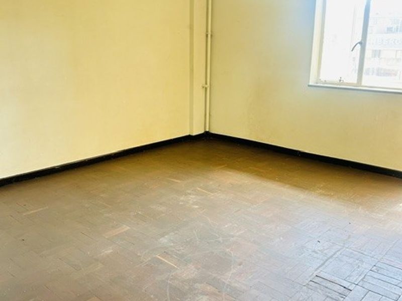 An empty bedroom featuring original parquet flooring, neutral wall finishes, and a sliding window, offering a blank canvas for renovation.