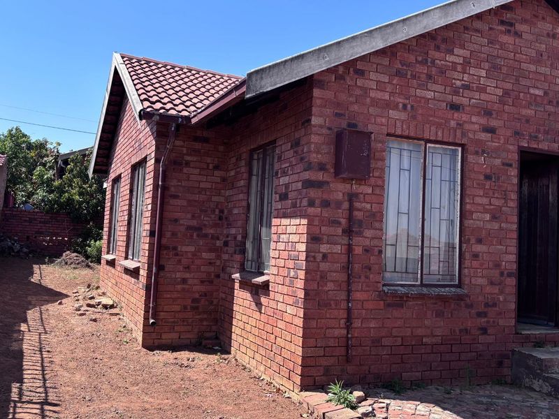 A side and rear view of a face brick house featuring a tiled roof, security bars on windows, and concrete entrance steps.