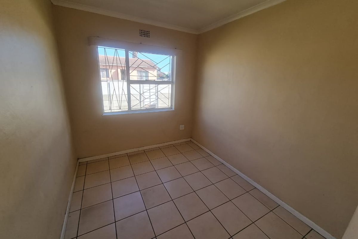 A vacant bedroom featuring neutral wall paint, tiled flooring, and a window fitted with security bars.