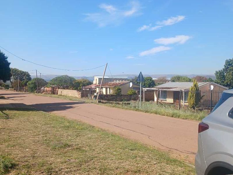 A street-level view of the neighbourhood approach, showing the paved road, surrounding residential properties, and perimeter fencing.