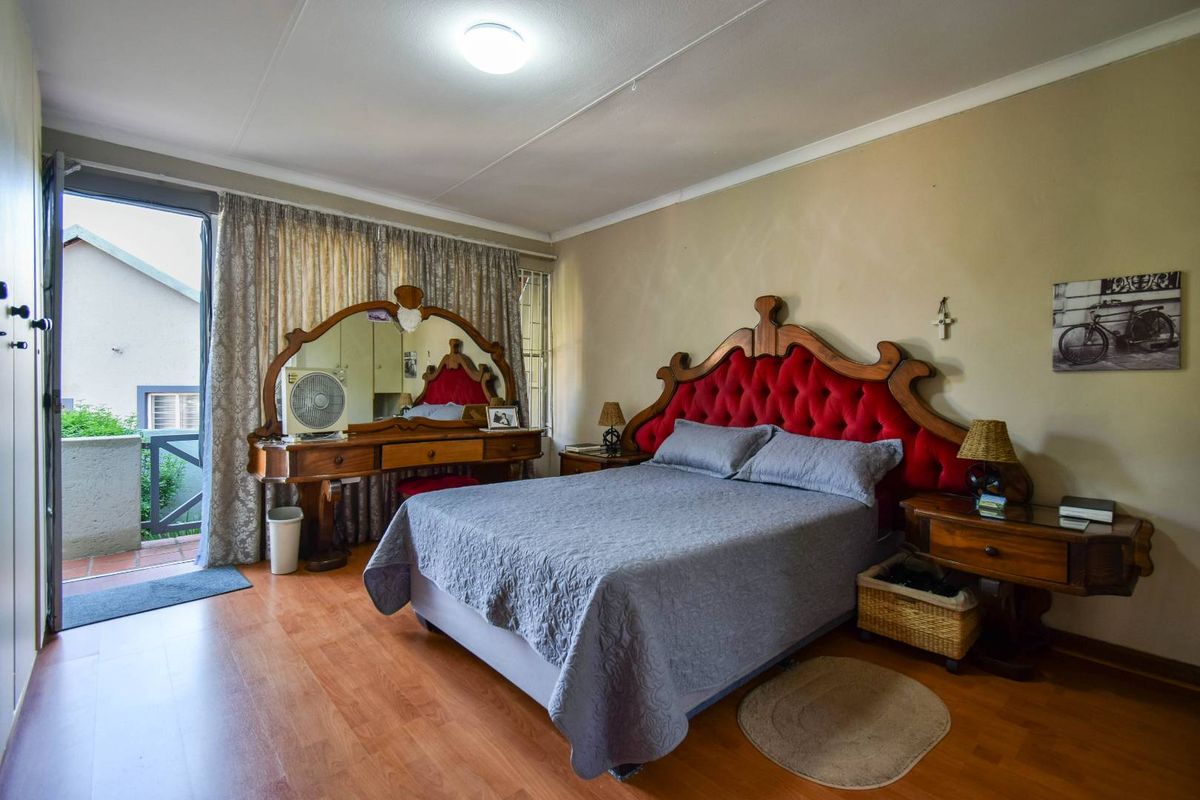 A bedroom featuring laminate flooring, built-in cupboards, and direct access to a private balcony through a glass door.