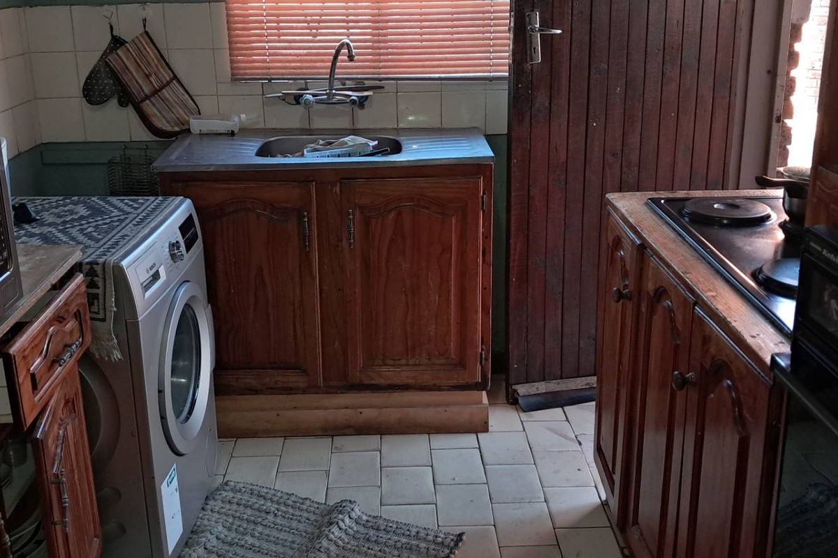A compact, dated kitchen featuring wooden cabinetry, a built-in oven and hob, and tiled flooring with direct access to an exterior door.