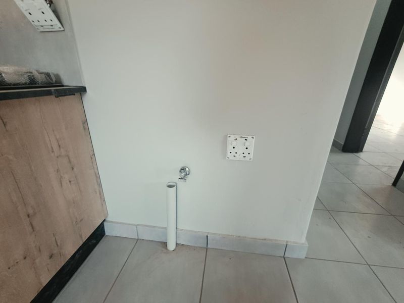A dedicated laundry utility area featuring plumbing connections, drainage pipe, and electrical power points, finished with neutral wall paint and tiled flooring.