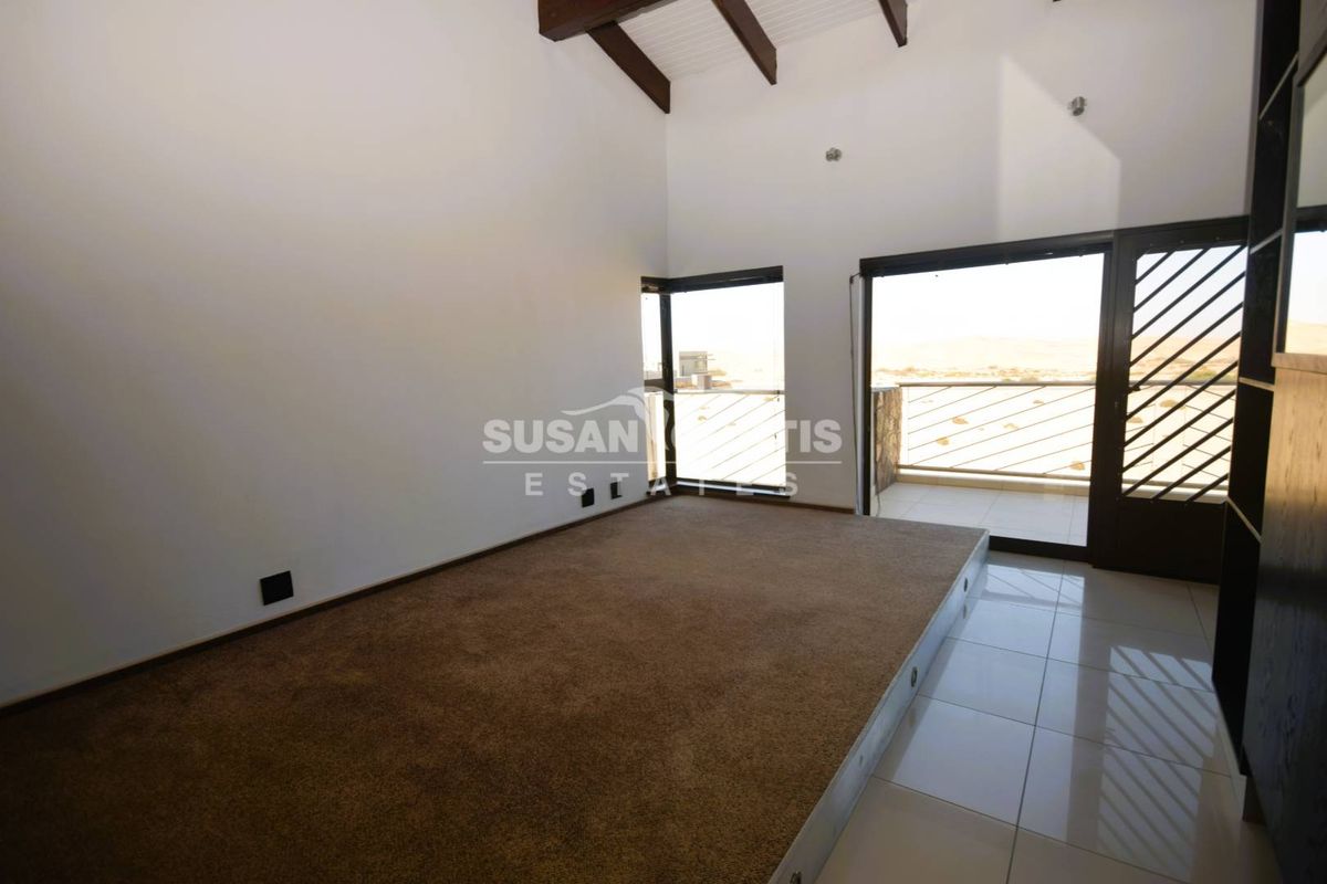 Spacious bedroom featuring a raised carpeted platform, vaulted ceilings with exposed beams, and direct access to a private balcony with scenic views.
