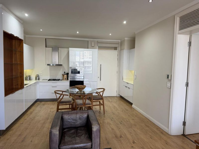 Modern open-plan kitchen and living area featuring sleek white cabinetry, integrated appliances, recessed lighting, and durable laminate flooring.