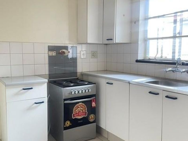 A functional kitchen featuring white cabinetry, tiled splashbacks, a freestanding stove, and a stainless steel sink with natural light from the window.