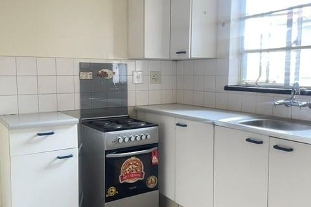 A functional kitchen featuring white cabinetry, tiled splashbacks, a freestanding stove, and a stainless steel sink with natural light from the window.