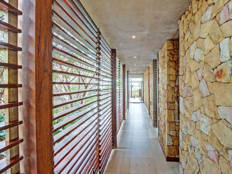 A modern, well-lit hallway featuring natural stone wall cladding and timber louvre screens that provide a unique architectural aesthetic.