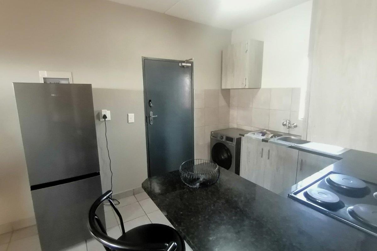 Compact kitchen featuring granite countertops, built-in cabinetry, an electric hob, and tiled backsplash, providing a functional workspace within the apartment.