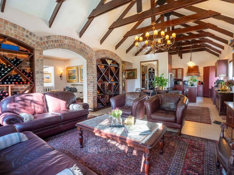 Spacious open-plan living area featuring vaulted ceilings with exposed timber beams, brick archways, and integrated wine storage, flowing into a functional kitchen space.