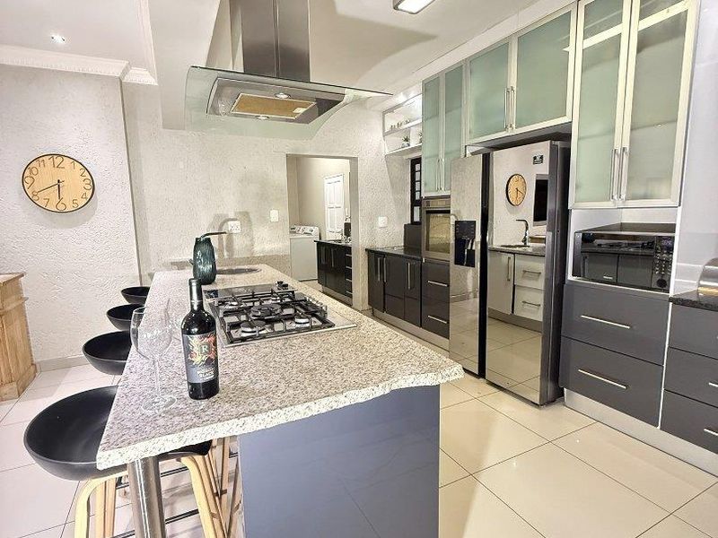 Modern kitchen featuring a central island with gas hob, granite countertops, sleek cabinetry, and integrated stainless steel appliances.