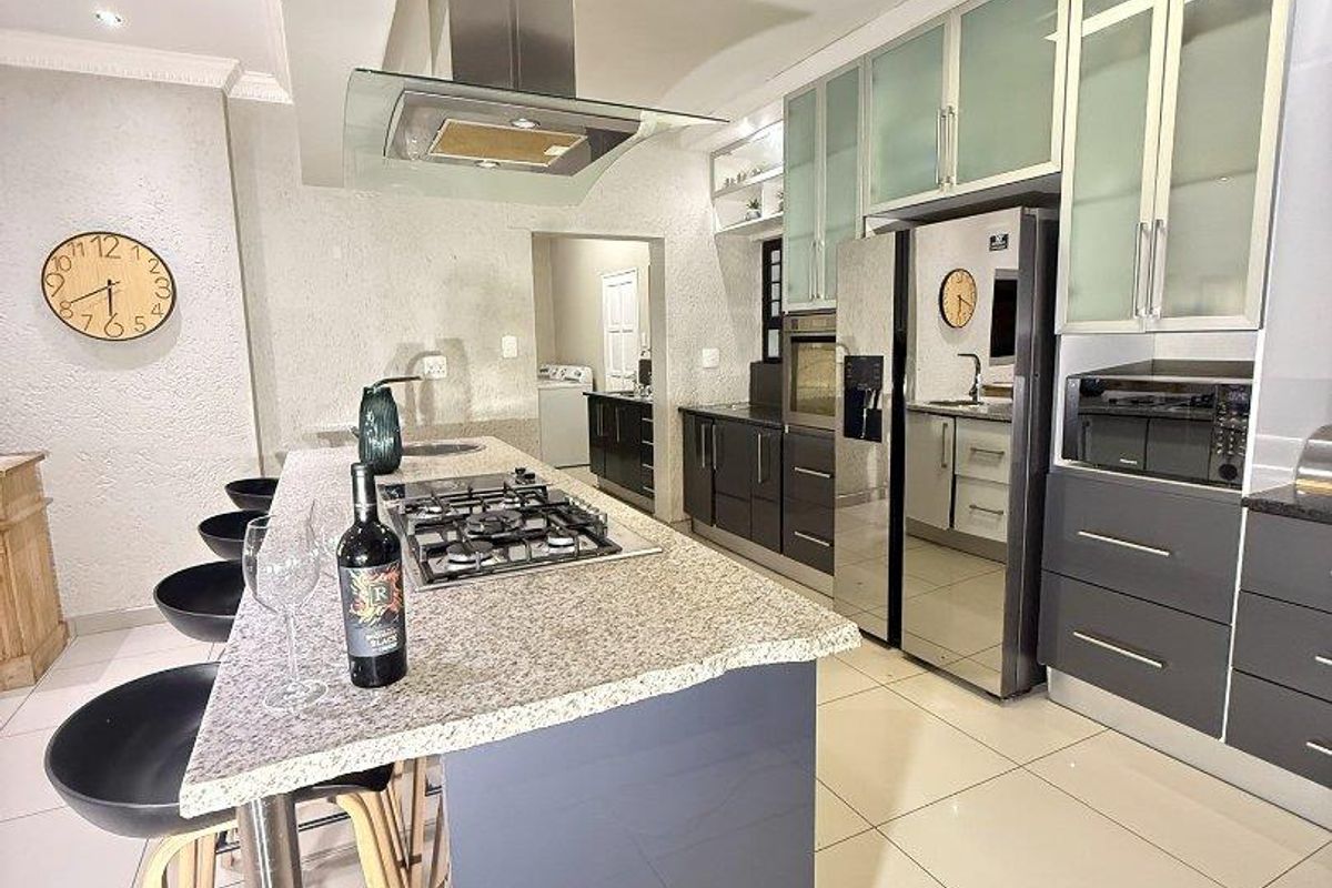 Modern kitchen featuring a central island with gas hob, granite countertops, sleek cabinetry, and integrated stainless steel appliances.