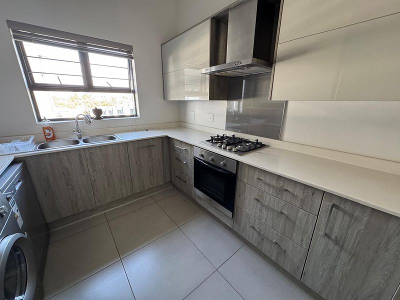 Modern kitchen featuring wood-grain cabinetry, stone countertops, integrated gas hob, oven, extractor fan, and a double stainless steel sink.