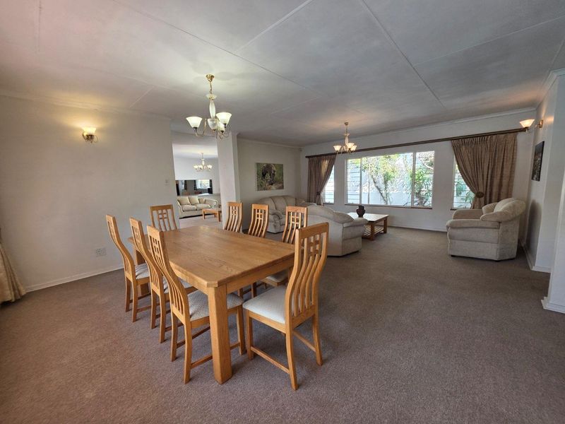 Spacious open-plan living and dining area featuring neutral carpeting, large windows for natural light, and traditional ceiling light fixtures.