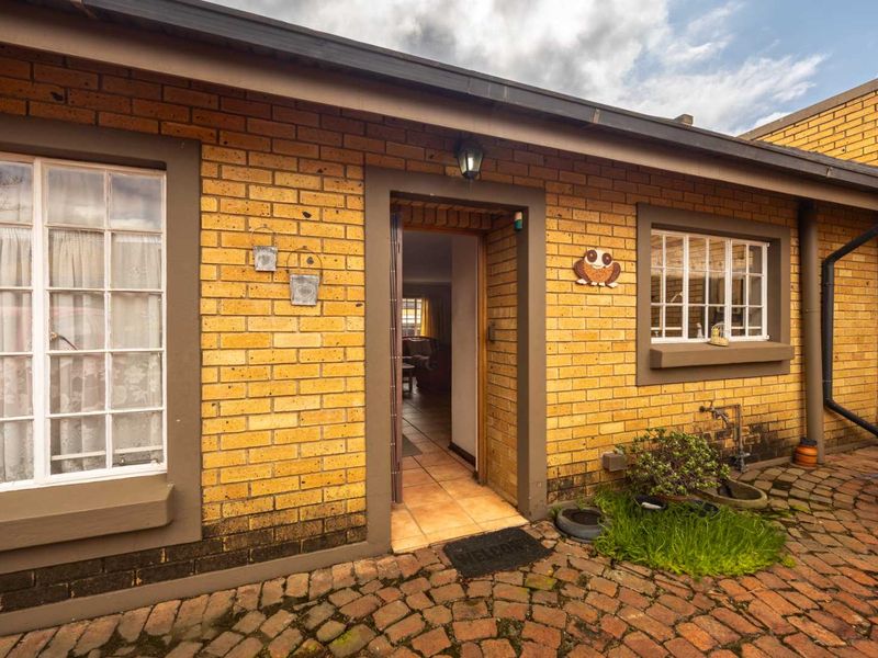 A rear exterior view of the house featuring a brick facade, tiled patio area, and access to the interior living space.