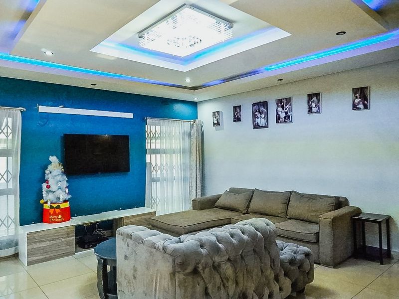 A modern living room featuring a recessed ceiling with integrated LED lighting, tiled floors, and large windows with security gates.