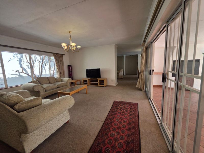Spacious living room featuring large windows, carpeted flooring, and sliding glass doors that provide direct access to the outdoor patio area.