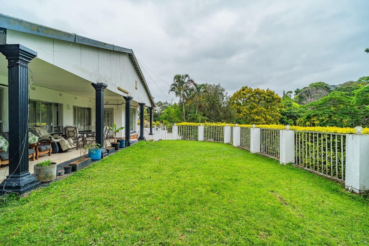 Rear view of the property featuring a covered patio with decorative columns, overlooking a spacious lawn and secure perimeter fencing.