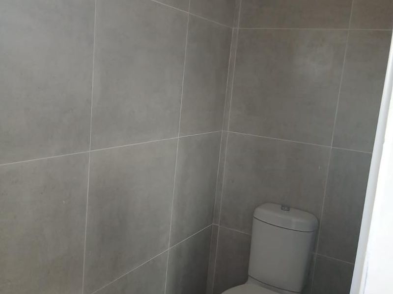 A compact, modern bathroom featuring neutral grey wall tiles and a standard white toilet.