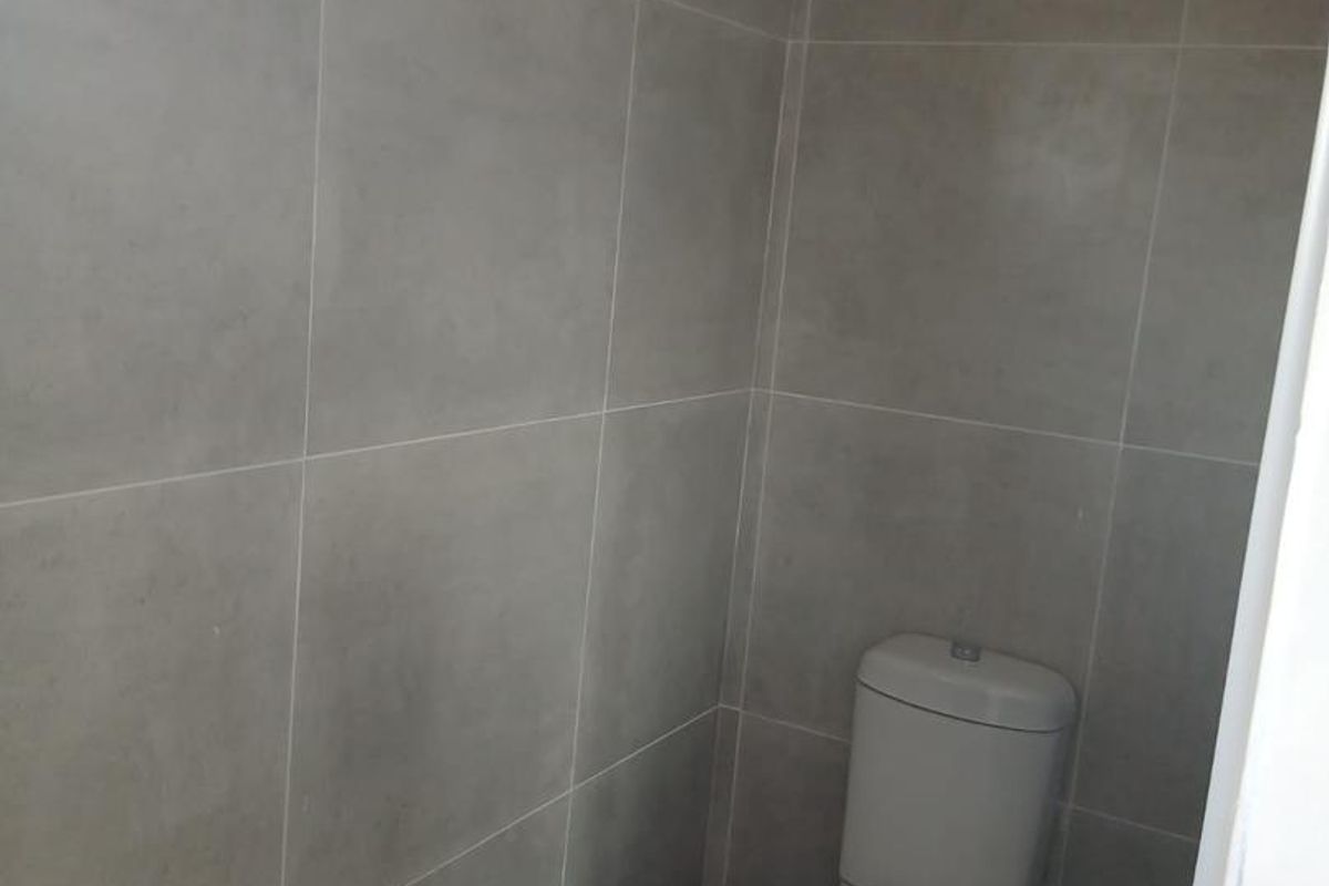 A compact, modern bathroom featuring neutral grey wall tiles and a standard white toilet.