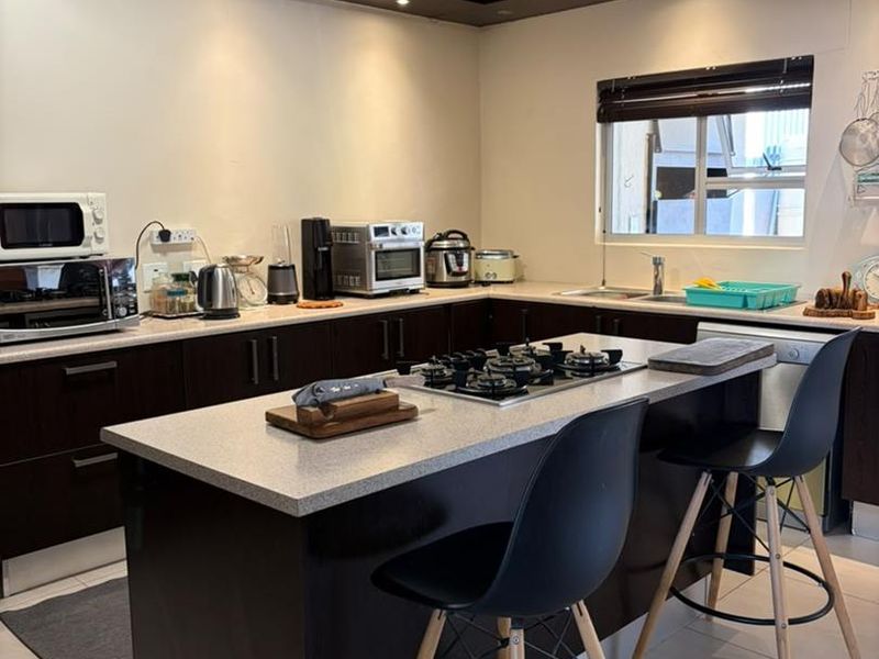 Modern kitchen featuring a central island with a gas hob, dark cabinetry, stone countertops, and recessed lighting.