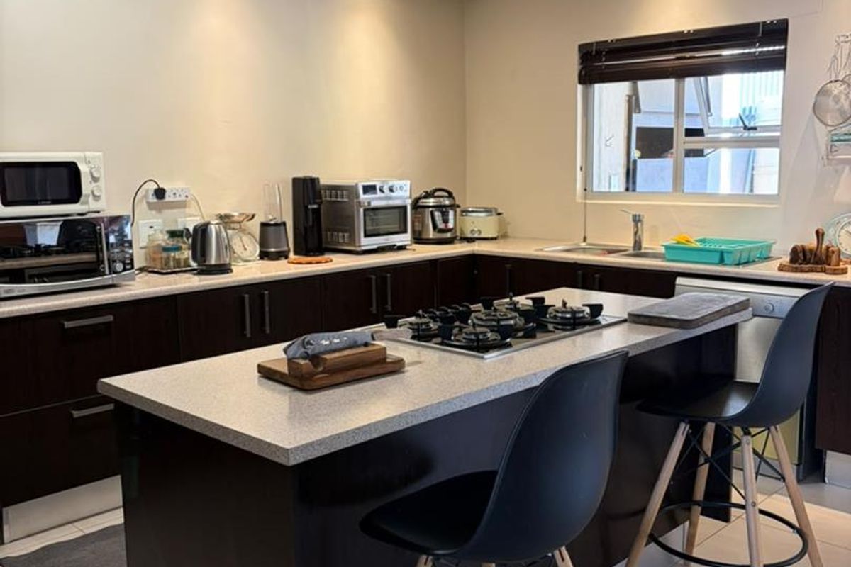 Modern kitchen featuring a central island with a gas hob, dark cabinetry, stone countertops, and recessed lighting.