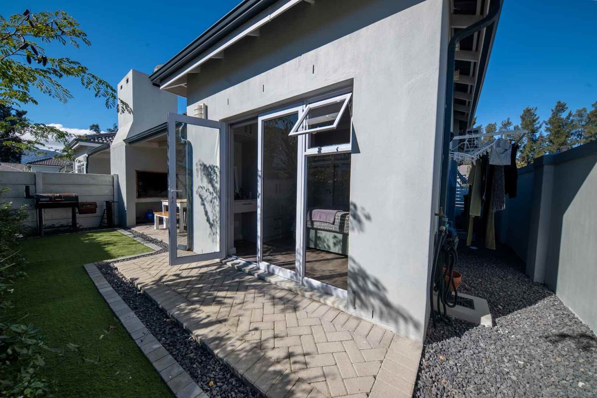 Rear exterior view featuring a paved patio, built-in braai area, and artificial lawn, providing a low-maintenance outdoor entertainment space.