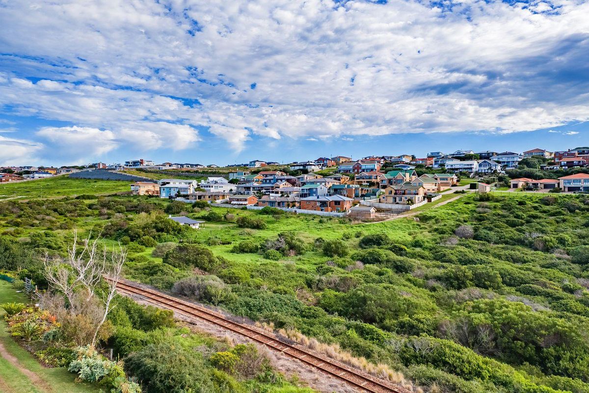 An aerial view of a residential area featuring natural vegetation and a railway track running through the landscape.