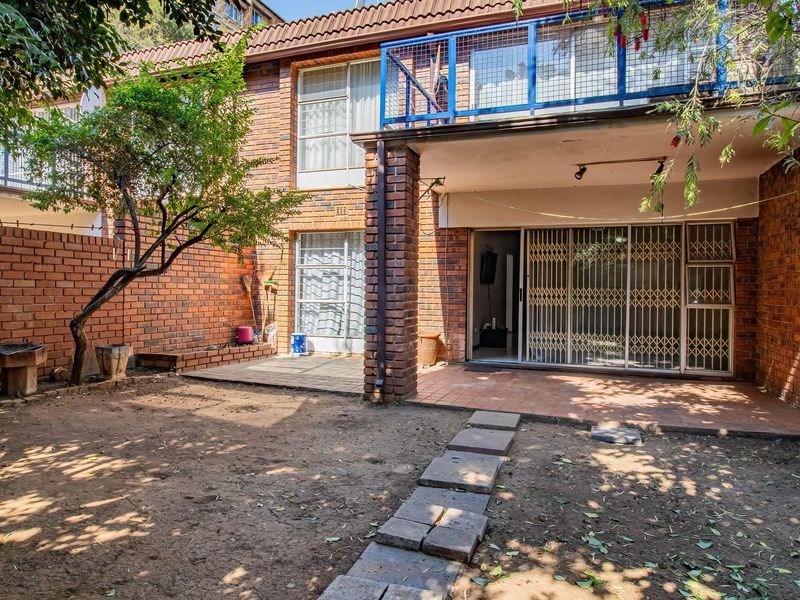 Rear exterior view of the apartment featuring a private garden, paved patio area, and a balcony with metal railings.