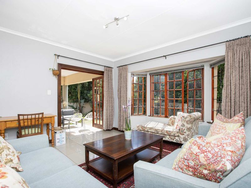 Bright living room featuring tiled floors, a large bay window with wooden frames, and direct access to an outdoor patio area through french doors.