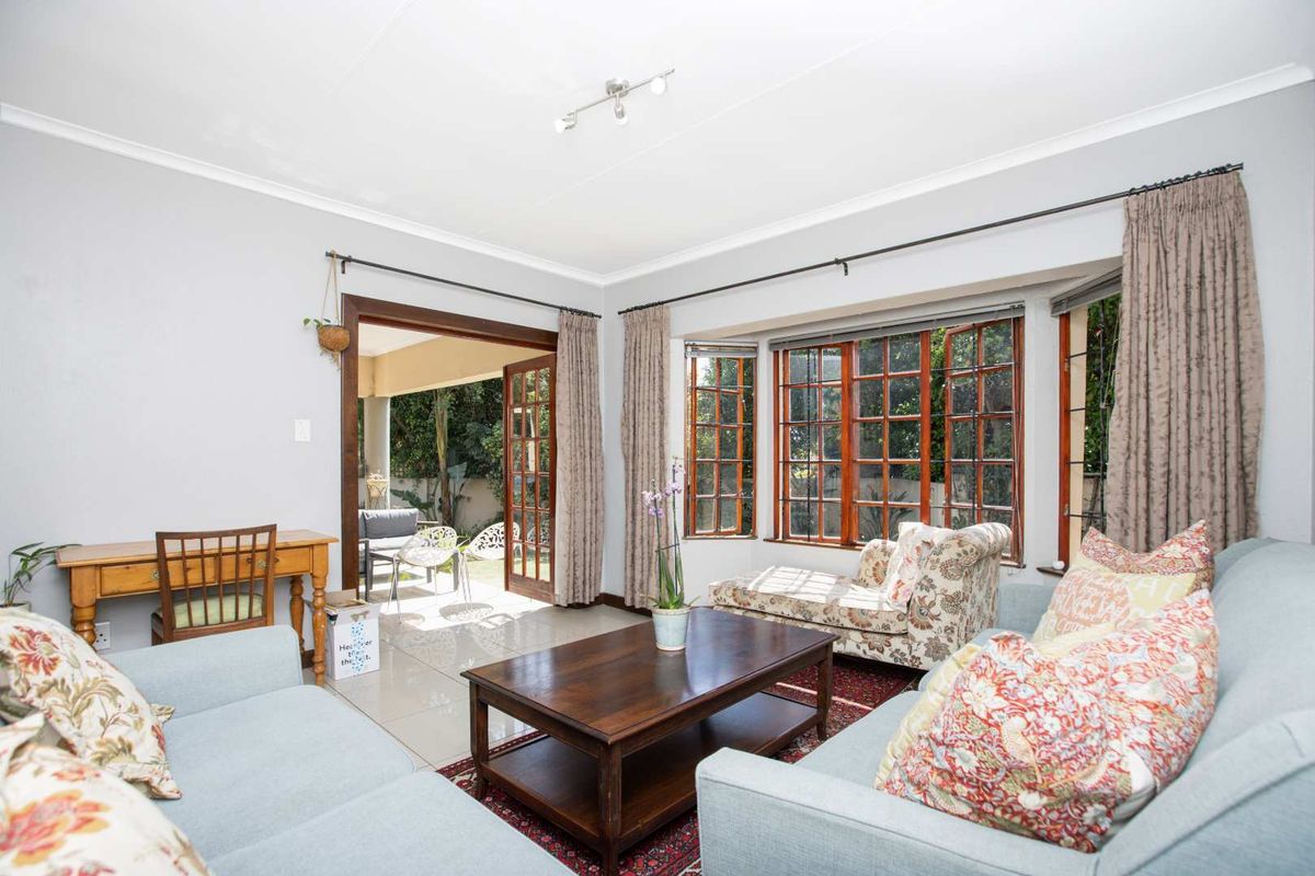 Bright living room featuring tiled floors, a large bay window with wooden frames, and direct access to an outdoor patio area through french doors.