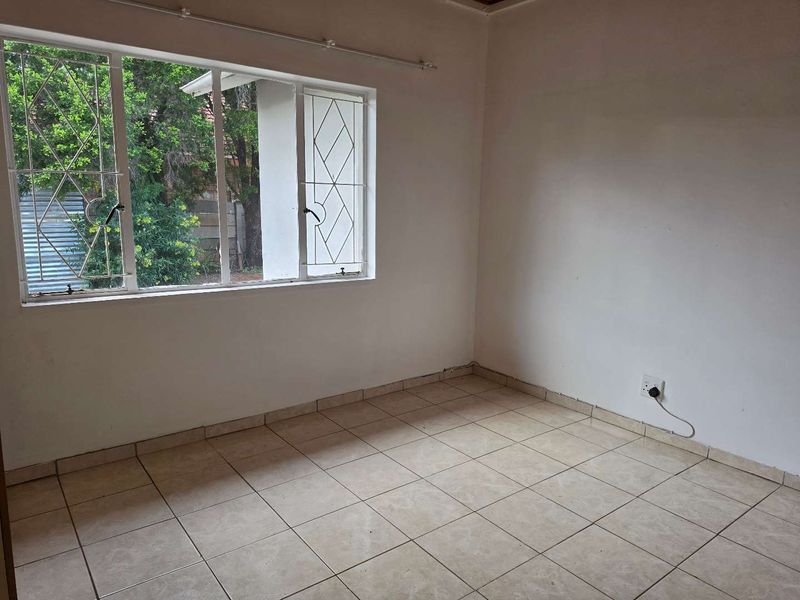 An empty bedroom featuring tiled flooring and windows fitted with security bars, offering a blank canvas for renovation.