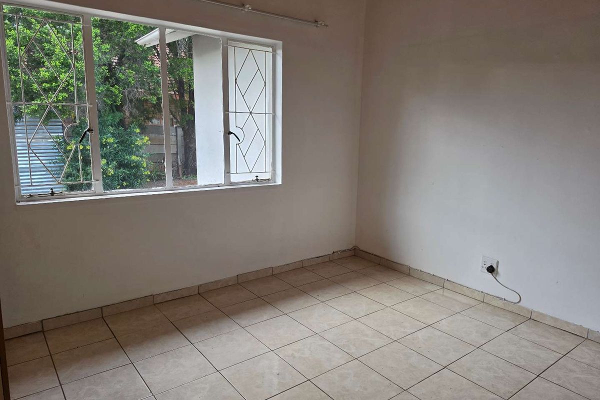 An empty bedroom featuring tiled flooring and windows fitted with security bars, offering a blank canvas for renovation.
