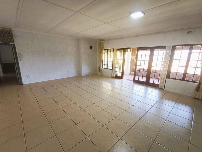 Spacious, empty living area featuring neutral tiled flooring and large wooden-framed glass sliding doors providing access to the outdoor patio area.